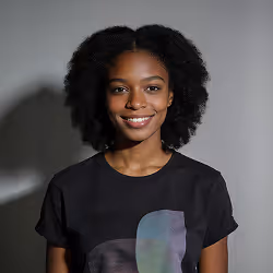 Smiling young woman with natural curly hair wearing a black shirt against a plain gray background.